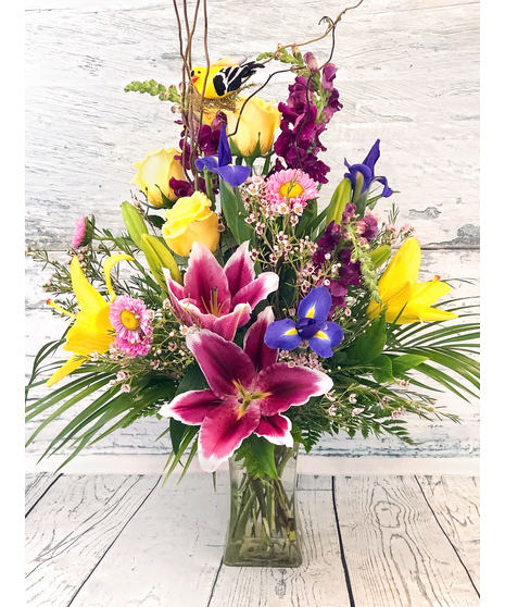 A beautiful garden style arrangement of spring colors! Stargazer lilies, iris, orchids and more are accented with ribbon, curly willow and a sweet spring bird.